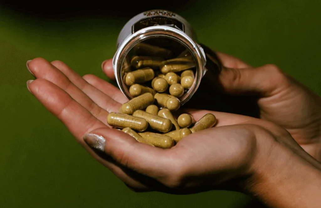 Kratom Capsules vs Kratom Liquid Shots shown in front of a green darkish background.