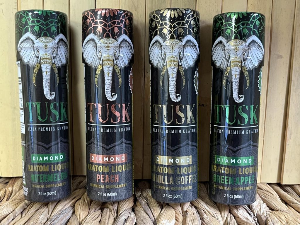 Four kratom shots displayed in front of a wooden background with wooden flooring below.