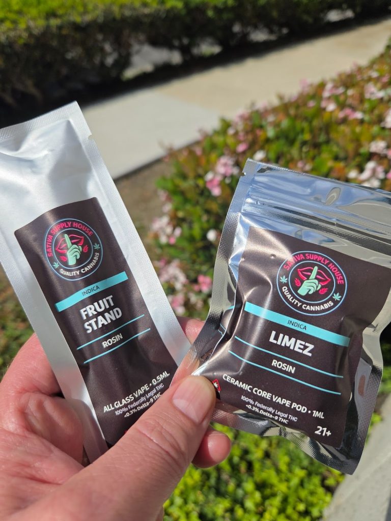 Sativa Supply House Live Rosin Vape Cart displayed in front of a  garden being held by someone.