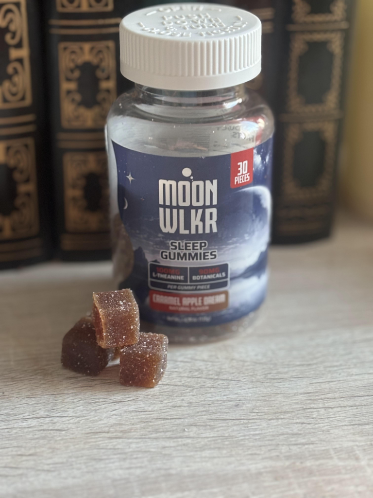 MOONWLKR Zero THC Sleep Gummies – Caramel Apple Dream displayed in front of books with three gummies displayed in front.
