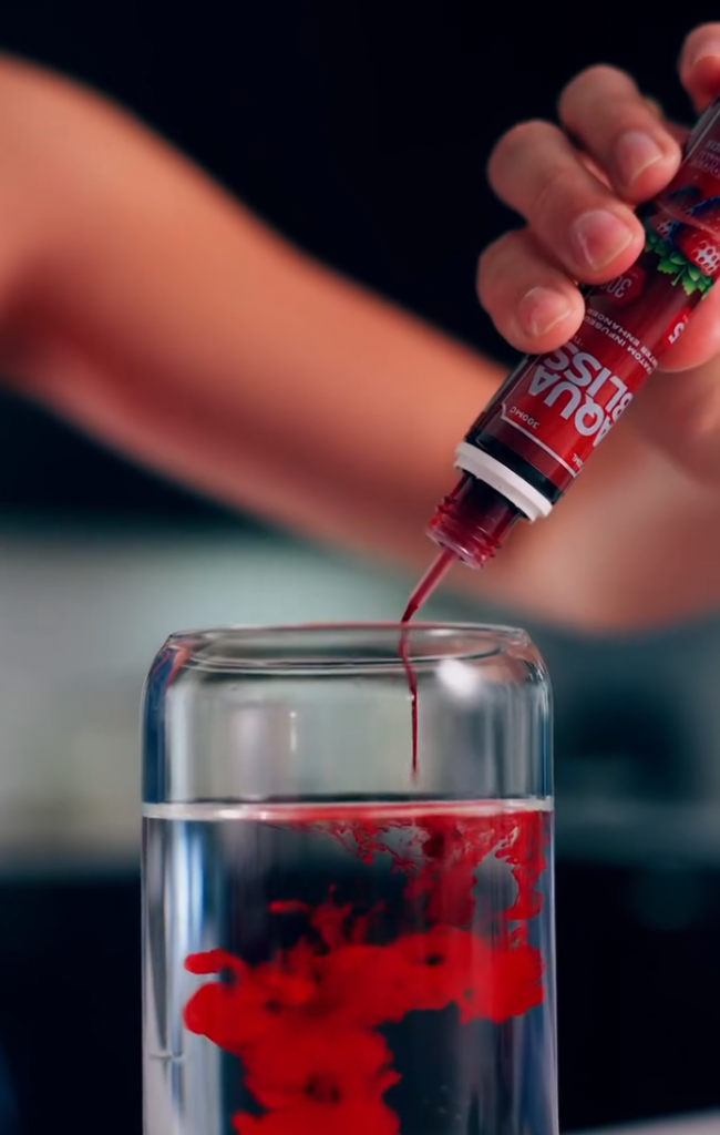 Kratom drink mix from Tusk Kratom being poured into a glass of water by a woman showing red liquid.