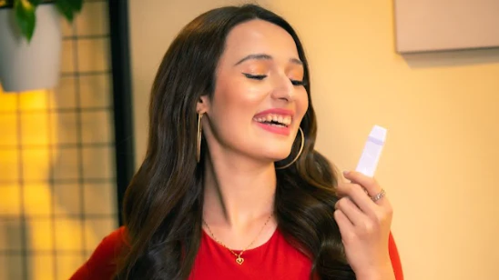 Woman holding a CAPNOS device showing how to buy pressurized air inhaler devices wearing a smile in front of a yellow background, a window, inside a room.