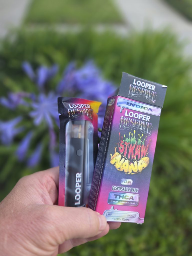 Looper Reserve 1G: Strawnana being held by a guy showing both the disposable vape and the box in front of a grassy area.