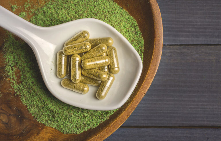 Kratom for pain showing the green powder and the capsule on a white spoon.