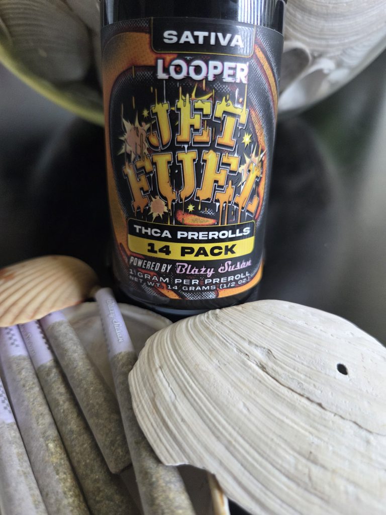Looper THCA Prerolls: Jet Fuel displayed in front of a bunch of stuff on top of a wooden table.