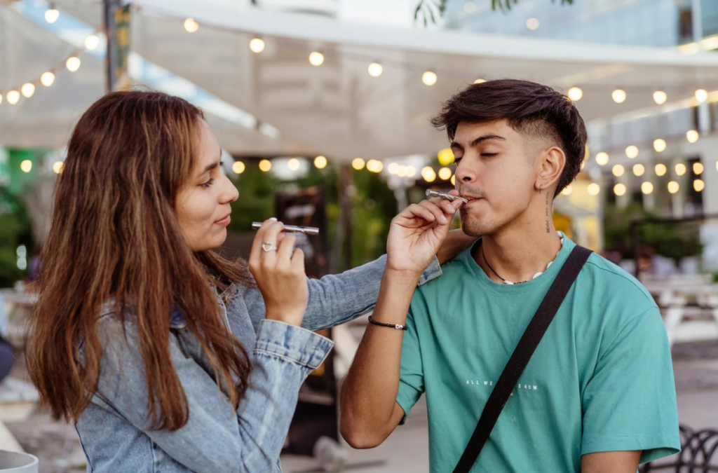 Vaporizer for Dry Herbs being used by a woman and a man in an outdoor setting with tents behind them and lights.