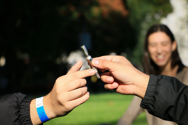 Vaporizer for Dry Herbs being used by a woman and a man in an outdoor setting with tents behind them and lights with a woman watching from behind.