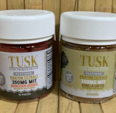 Kratom vs Kava shown by Tusk Kratom products displayed in front of a wooden wall and on top of a wooden floor.