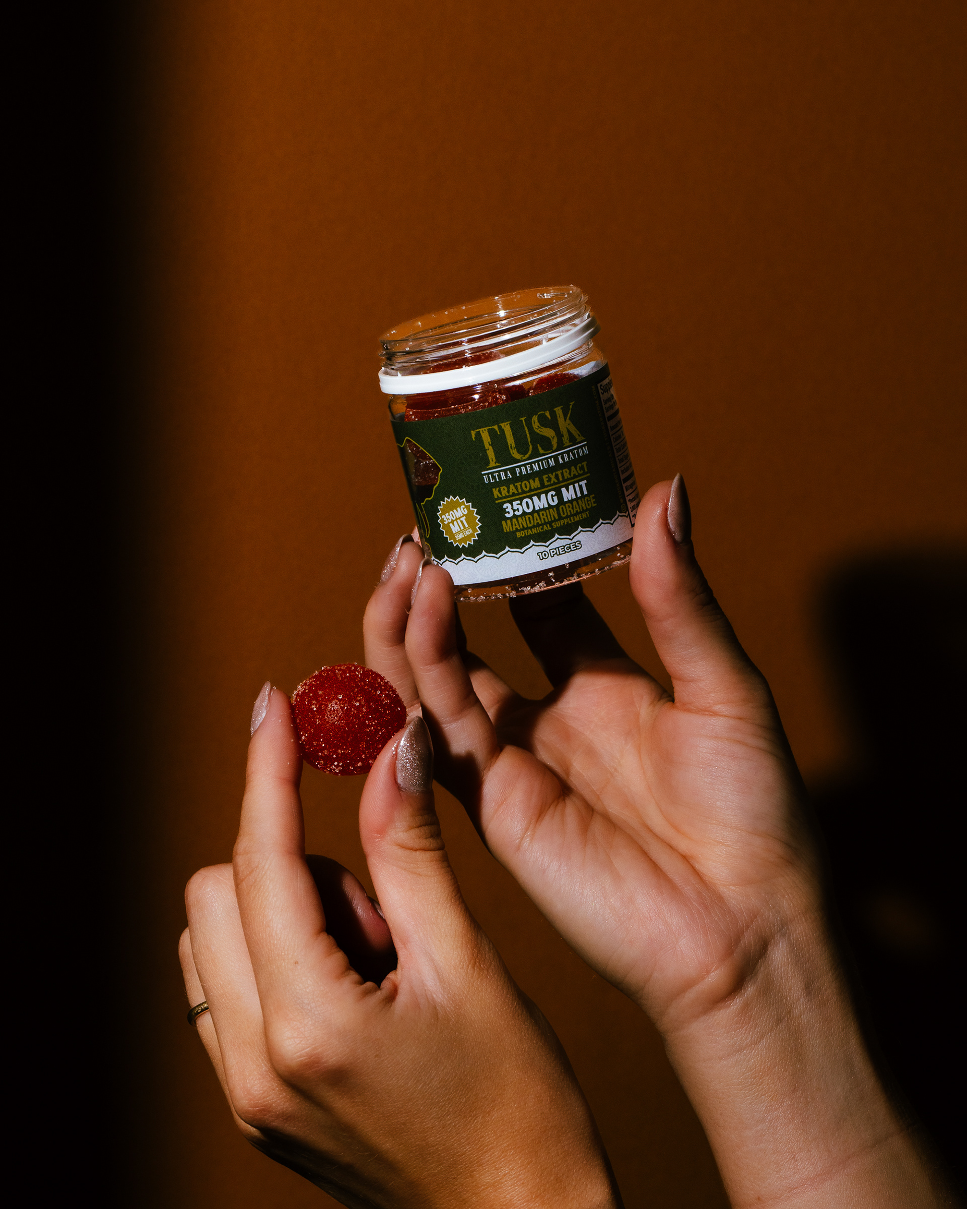 Single-serve kratom being held by a person in front of a brown and orange background while also holding a cherry on her left hand.
