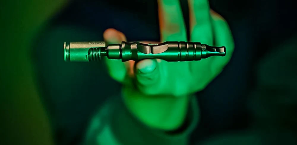 Long Lasting Dry Herb Vaporizers by DYNAVAP one of them being held by someone inside a green background and illuminated by green light.