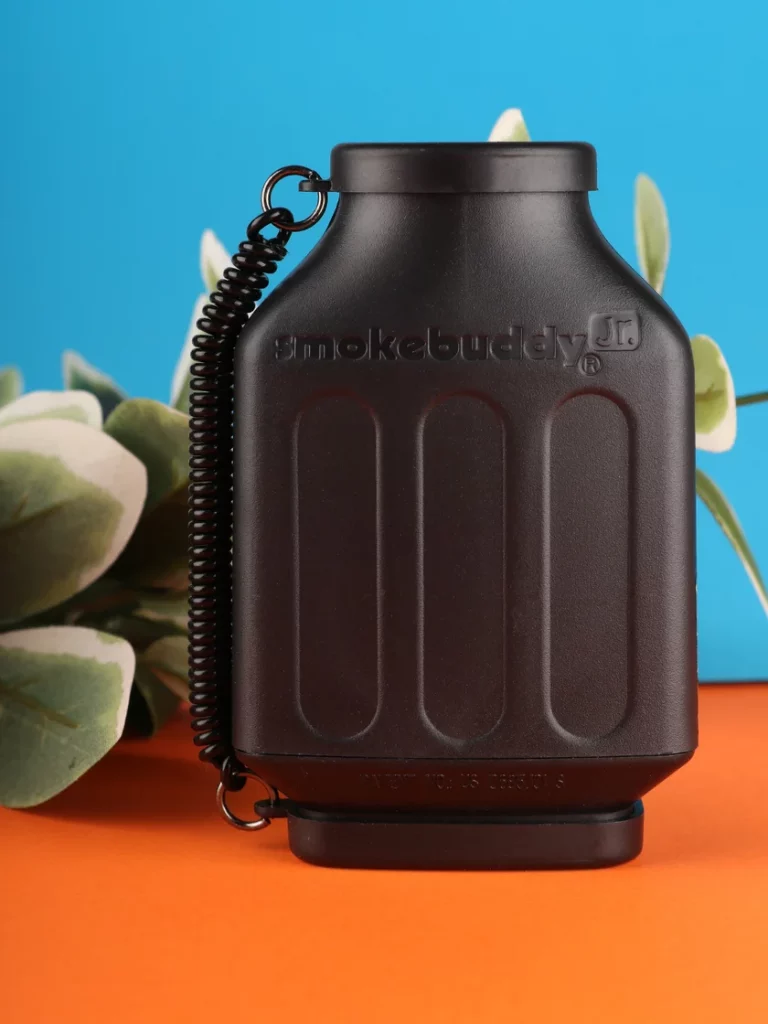 How to smoke discreetly being shown by a black Smokebuddy device displayed on top of an orange table beside a green banana in front of a blue background.