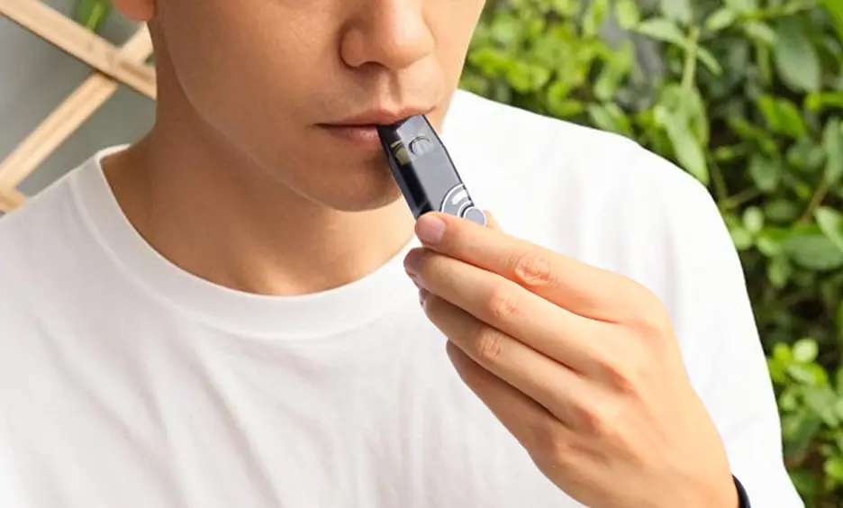 Qutting vape now shown by a man using a CAPNOS Zero device while wearing a white shirt, outdoors in front of a bush.