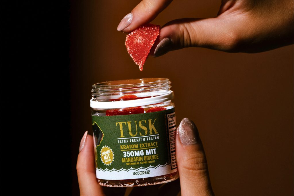 Kratom shot being used as a dip for a fruit held by a person in front of a brown background.