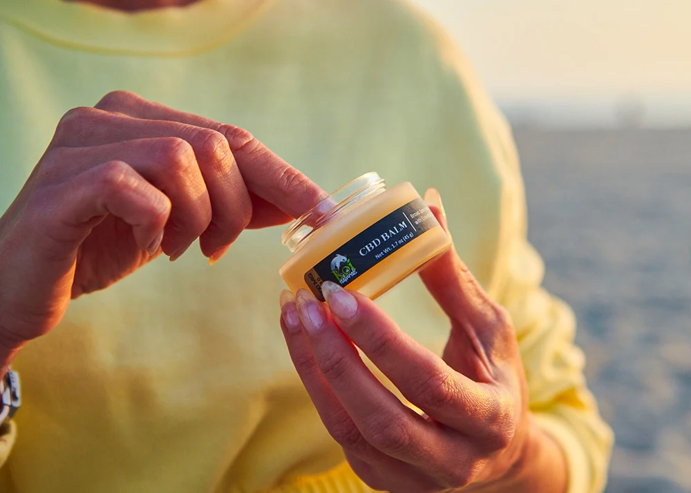 CBD balm being used by a guy in lime green shirt in front of a beach background.