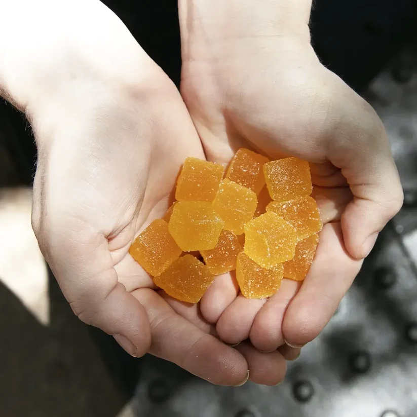 MOONWLKR CBD: CBN : THC Sleep Gummies — Totally Tropical held by someone in the air showing the gummies.